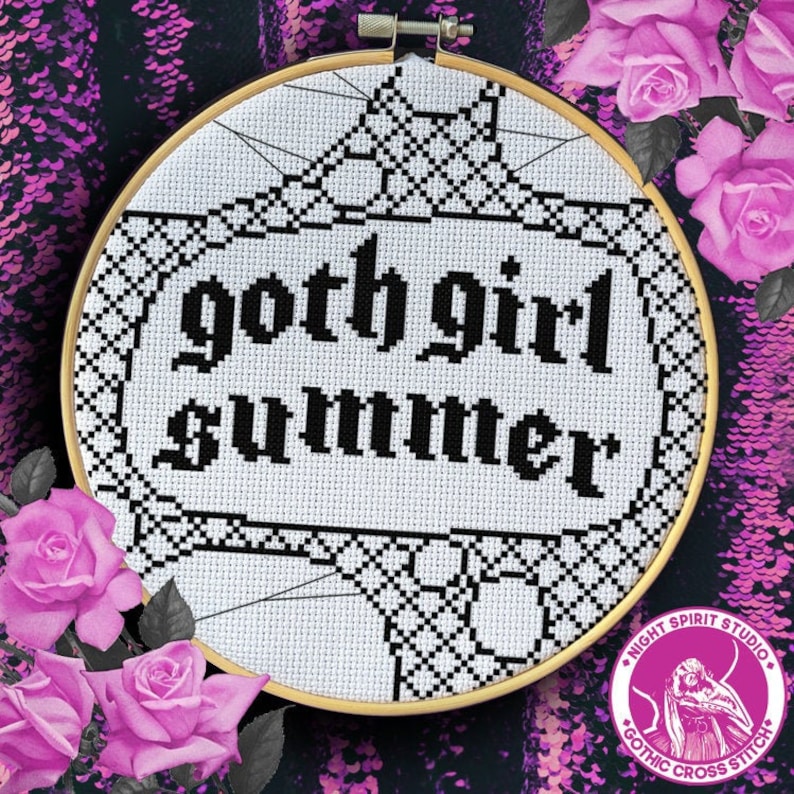 May include: A white cross stitch embroidery hoop with black thread. The design features a gothic font that reads "goth girl summer" with a black lace pattern around the text.
