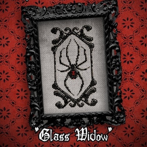 May include: Black and white cross-stitch embroidery of a black widow spider in a black frame with the text "Glass Widow" below the frame.