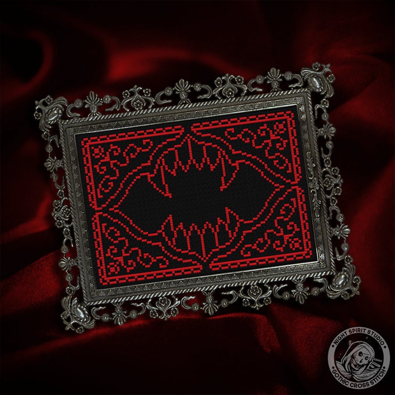 May include: A framed cross-stitch design featuring a red bat with intricate details on a black background. The frame is silver with a decorative design.