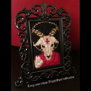 Pode incluir: Uma moldura preta adornada com uma imagem de ponto cruz de uma cabra com um pentagrama vermelho na testa. A cabra está vestindo uma túnica vermelha e preta. A moldura está em um suporte e o texto "Etsy.com/shop/NightSpiritStudio" é visível na parte inferior.
