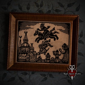 May include: A framed cross-stitch embroidery depicting a black silhouette of a witch riding a horse over a city skyline. The embroidery is on a beige fabric and the frame is brown wood.