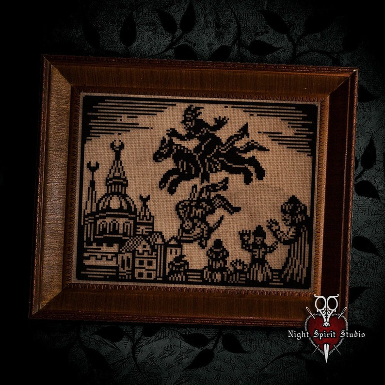 May include: A framed cross-stitch embroidery depicting a black and white scene of witches flying over a town. The witches are riding on broomsticks and horses. The town has a church with a steeple and other buildings. The embroidery is on a beige fabric and is framed in a dark brown wood frame.
