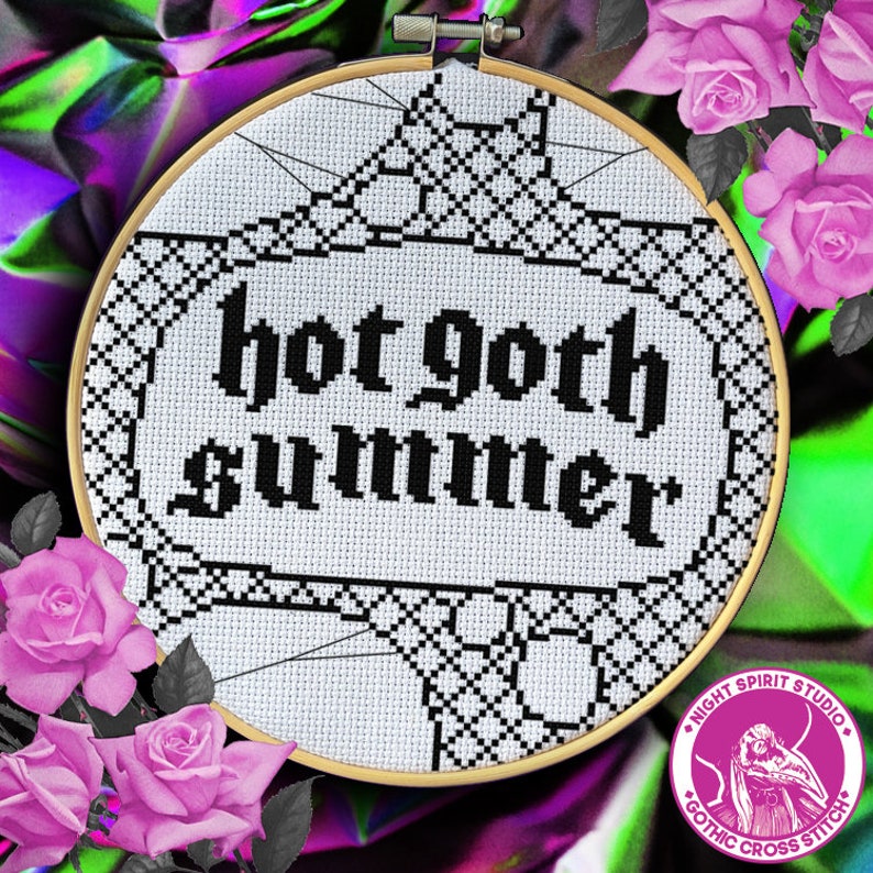 May include: A white cross-stitch embroidery hoop with black thread, featuring the text "hot goth summer" in a gothic font. The hoop is surrounded by pink roses.