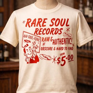 May include: Off-white t-shirt featuring red text and graphics. The design reads "RARE SOUL RECORDS" with additional text: "R&B-SOUL-FUNK", "RAW & AUTHENTIC!", and "OBSCURE & HARD TO FIND." The shirt has a cartoon image of a man holding a sign.