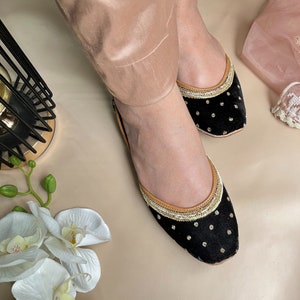 May include: A pair of black velvet flats with gold trim and white polka dots. The flats have a pointed toe and a low heel.
