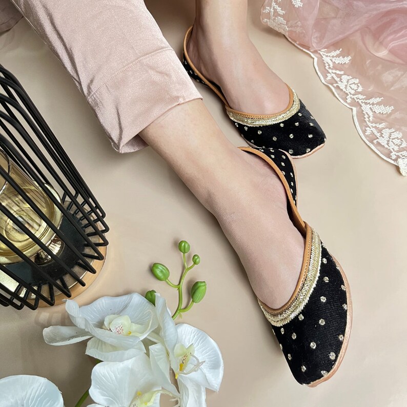 May include: A pair of black velvet flats with gold polka dots and gold trim. The flats have a pointed toe and a low heel.