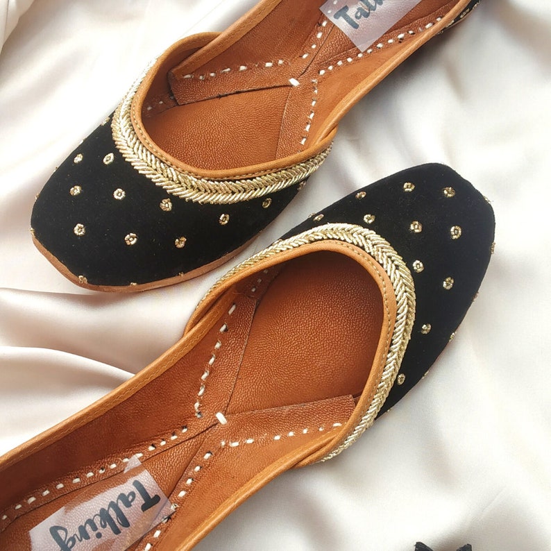 May include: A pair of black velvet shoes with gold embroidery and a brown leather insole. The shoes have a pointed toe and a low heel. The brand name "Tallinn" is visible on the insole.