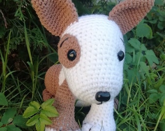 May include: A handmade crochet dog toy with a white body, brown ears, and brown patches around the eyes. The dog has black eyes and a black nose. The text "Bear Of Good" is in white script above the dog.