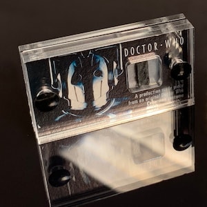 Peut inclure: Un présentoir en acrylique transparent avec un morceau de costume Cyberman de Doctor Who. Le boîtier présente un graphisme noir et blanc d'un Cyberman et les mots "Doctor Who". Le texte indique "Une pièce de production issue d'un costume Cyberman original de Doctor Who."