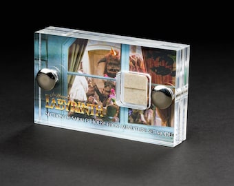 Könnte beinhalten: Eine transparente Acryl-Vitrine mit einem Abschnitt von Sarahs Haus aus dem Film Labyrinth. Die Vitrine zeigt ein kleines, weißes, rechteckiges Stück des Set-Modells sowie ein gedrucktes Bild des Hauses und den Filmtitel.