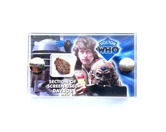 May include: A clear plastic display case with a section of screen-used Davros from the Doctor Who television series. The case also features a photo of the Fourth Doctor, Tom Baker, and a Dalek.