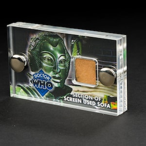 May include: A clear acrylic display case with a section of screen used in the Doctor Who television series. The case features a close-up of the character, the Doctor Who logo, and the text "SECTION OF SCREEN USED SOFA".