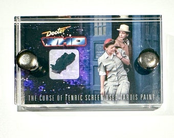 May include: A clear acrylic display case with a black and white image of a scene from the Doctor Who television series. The image shows two characters, a woman and a man, standing in front of a blue police box. The text "Doctor Who" is printed in red and white on the top of the case. The text "The Curse of Fenric Screen Used Tardis Paint" is printed on the bottom of the case.