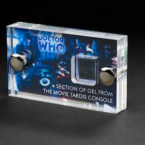 Könnte beinhalten: Eine transparente Acrylglas-Vitrine mit einem Abschnitt Gel aus der TARDIS-Konsole des Films. Die Vitrine zeigt ein Foto der Doctor Who-Besetzung und den Text "DOCTOR WHO" und "SECTION OF GEL FROM THE MOVIE TARDIS CONSOLE".