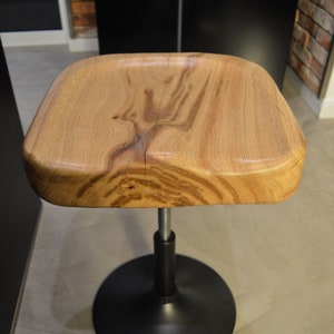 May include: A wooden stool with a natural wood finish and a black metal base. The stool has a unique, organic shape.