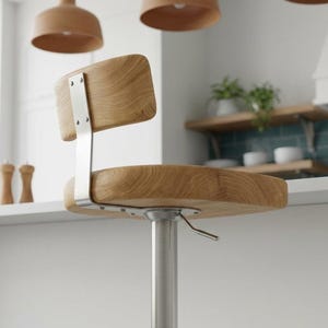 Puede incluir: Un taburete de bar con asiento y respaldo de madera clara con veta visible. El asiento se apoya en una columna central de metal cepillado, un reposapiés circular y un soporte metálico vertical que conecta el asiento con el respaldo.