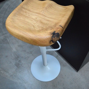 Handcrafted wooden counter stool featuring a comfortable, contoured saddle seat with a beautiful rustic wood split. Adjustable black pedestal base with sleek footrest. Two minimalist kitchen counter stools styled in a warm, inviting modern farmhouse interior.