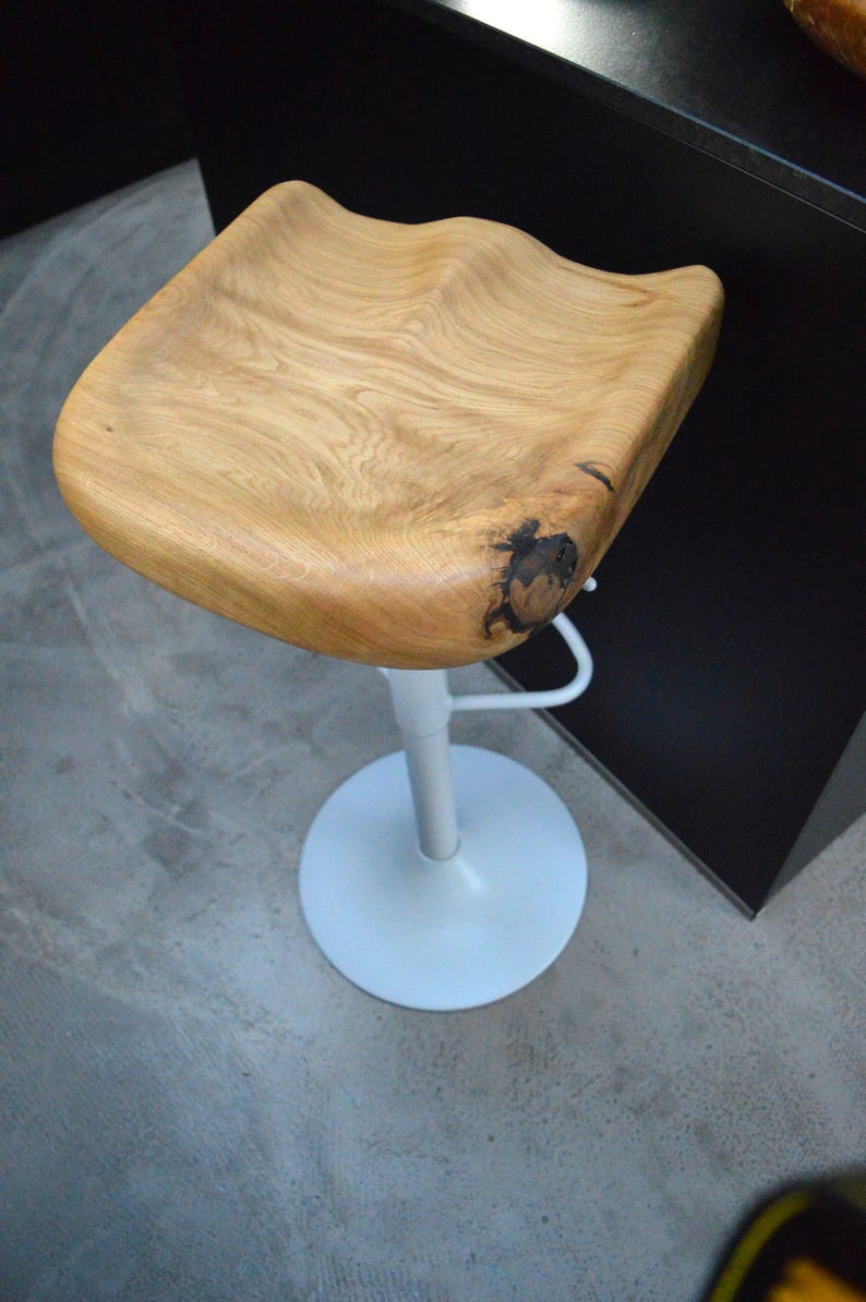 Handcrafted wooden counter stool featuring a comfortable, contoured saddle seat with a beautiful rustic wood split. Adjustable black pedestal base with sleek footrest. Two minimalist kitchen counter stools styled in a warm, inviting modern farmhouse interior.