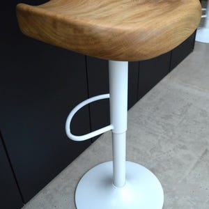 Minimalist oak counter stool featuring a heavy, thick-cut solid wood seat with rich natural texture and an organic shape. Matte black powder-coated metal base with integrated footrest. Two luxury counter height stools perfectly styled for a clean, upscale modern kitchen design.