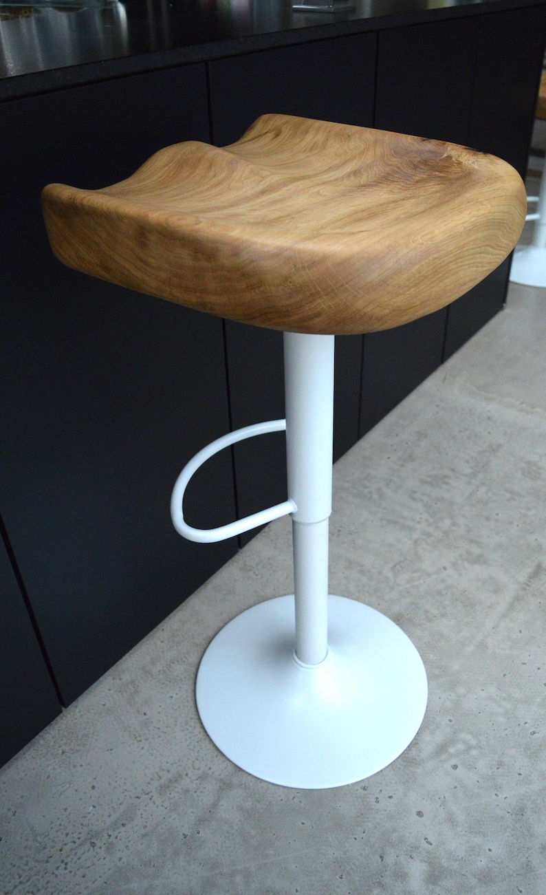 Minimalist oak counter stool featuring a heavy, thick-cut solid wood seat with rich natural texture and an organic shape. Matte black powder-coated metal base with integrated footrest. Two luxury counter height stools perfectly styled for a clean, upscale modern kitchen design.