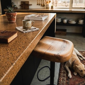 Sculpted wood counter stool made of solid oak with rustic live edge details. Contemporary kitchen island seating with a matte black adjustable base. Elegant modern farmhouse kitchen decor featuring high-quality handcrafted wooden furniture.
