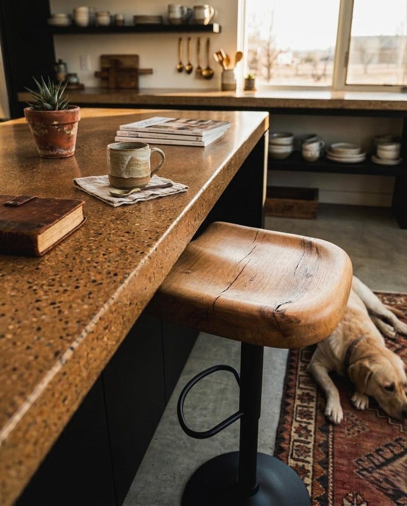 Sculpted wood counter stool made of solid oak with rustic live edge details. Contemporary kitchen island seating with a matte black adjustable base. Elegant modern farmhouse kitchen decor featuring high-quality handcrafted wooden furniture.