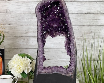 May include: A large amethyst geode with a natural opening, revealing a purple crystal interior. The geode is mounted on a black base.