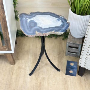 May include: A unique side table with a natural agate stone top in shades of blue, white, and brown. The stone is supported by a black, three-legged metal base. This decorative table adds a touch of natural elegance to any living space.