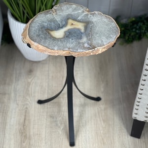 May include: A small, round, agate table with a natural, light brown, gray, and white pattern. The table has a black metal base with three legs.