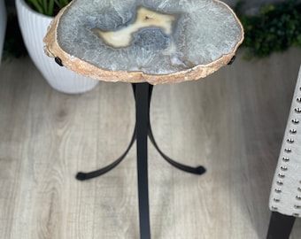 May include: A small, round, agate table with a natural, light brown, gray, and white pattern. The table has a black metal base with three legs.