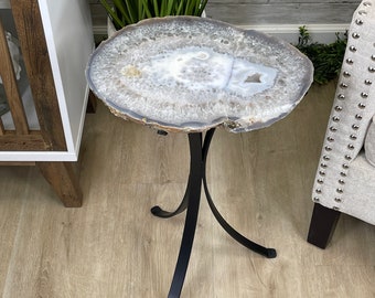 May include: A white agate slice table top with a natural edge, supported by a black metal tripod stand. The table is on a light brown wood floor.