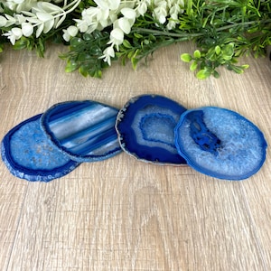 May include: Four blue agate coasters with different patterns. The coasters are round and have a natural, polished finish.