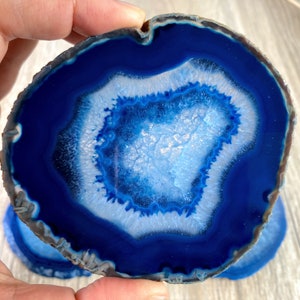May include: A blue agate slice with a white center and a dark blue outer edge. The agate is smooth and polished, and it has a natural, organic shape.