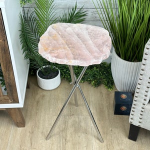 May include: A pink crystal side table with a unique, irregular shape and a silver metal tripod base.