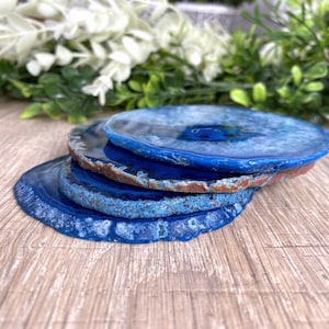 May include: Four blue agate coasters stacked on top of each other. The coasters are round and have a natural, polished finish.