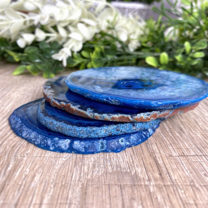 May include: Four blue agate coasters stacked on top of each other. The coasters are round and have a natural, polished finish.