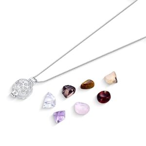 May include: A silver necklace with a cage pendant and a variety of colorful gemstones. The gemstones include amethyst, rose quartz, and other polished stones in shades of brown, red, and clear.