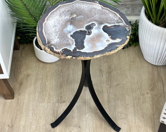 May include: A black metal side table with a round agate top. The agate is a light brown and white colour with a swirling pattern.