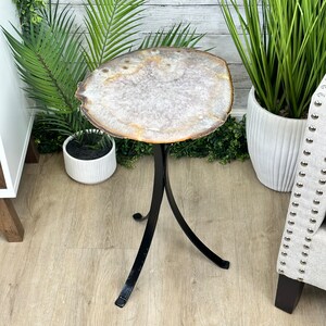 May include: A white agate slice table top with a black metal tripod base. The table top is a natural stone with a unique pattern. The base is made of sturdy metal and has a sleek, modern design.