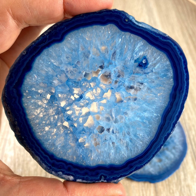 May include: A blue agate slice with a white center and a dark blue outer edge. The agate is polished and has a smooth surface.