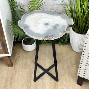 May include: A side table with a natural agate stone top. The stone has a white and blue pattern. The table has a black metal base with an X-shaped support. The table is approximately 61 cm tall.
