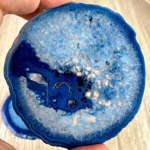 May include: A blue agate coaster with a white and blue crystal pattern. The coaster is round and has a smooth, polished surface.