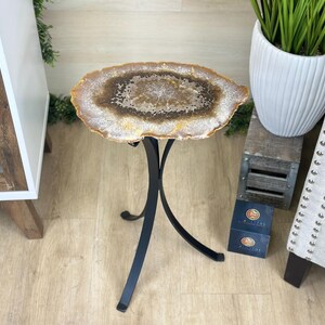 May include: A unique side table with a natural agate stone top. The stone features a brown and white pattern with a gold edge, supported by a black metal base. The table is a decorative accent piece.