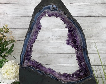 May include: A large amethyst geode with a natural heart-shaped opening. The geode is dark purple and has a black base.