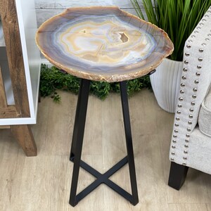 May include: A small, round agate table with a natural brown, white, and blue pattern. The table has a black metal base with a cross-shaped design.