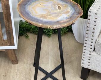 May include: A small, round agate table with a natural brown, white, and blue pattern. The table has a black metal base with a cross-shaped design.
