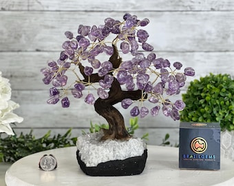Könnte beinhalten: Amethyst-Kristallbaum mit Drahtgestell und natürlichem Holzsockel. Der Baum steht auf einem weißen Quarzsockel und einem schwarzen Sockel. Der Baum ist etwa 30 cm hoch.