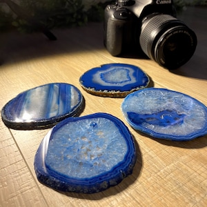 May include: Four blue agate coasters with white and blue patterns. The coasters are round and have a natural, polished finish.