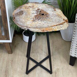 May include: A round, light brown agate table top with a black metal base. The base is a triangular shape with a crossbar in the middle.