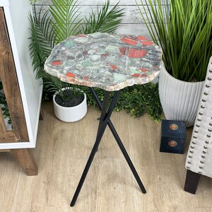 May include: A small, round side table with a unique, green, red, and white agate stone top. The table has a black metal tripod base.